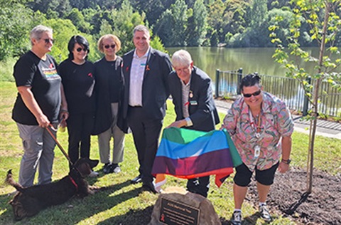 A group of people standing around the memorial with the rainbow flag unveiling the plaque